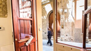 A wooden door with a newspaper rack, a stone wall, and a person walking outside. - Arc Home - The charm of living in the heart of Castello, the oldest neighborhood. (Cagliari)