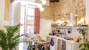 A rustic kitchen with exposed beams, a stone wall, and a dining area with a table and chairs. - Arc Home - The charm of living in the heart of Castello, the oldest neighborhood. (Cagliari)