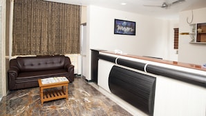 A reception area with a brown leather sofa, a wooden coffee table, a reception desk, a framed picture on the wall, and a ceiling fan. - Hotel Rathnavel Towers (Chennai)