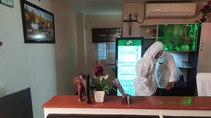 A reception desk with a vase of flowers, a framed picture on the wall, and a refrigerator in the background. - Hotel Rathnavel Towers (Chennai)