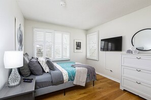 Un dormitorio con cama, cómoda, televisor y lámpara.