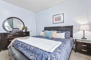 A bedroom with a bed, a dresser, a mirror, a bedside table, and a lamp.