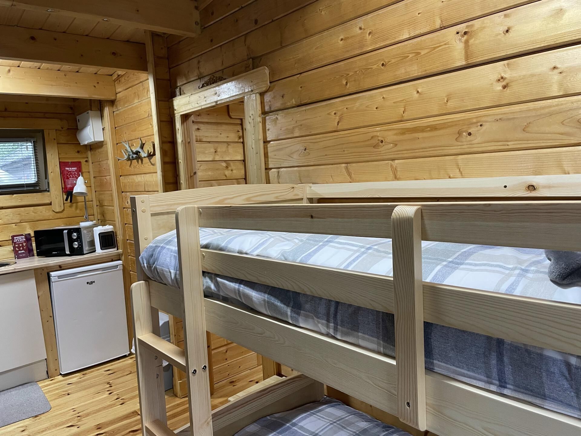 Interior de una cabaña de madera con literas, una kitchenette y una ventana con persianas.
