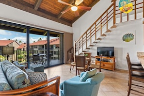 Relax in this spacious living area with a sofa set, dining table, and TV, leading to an outdoor patio with a view.