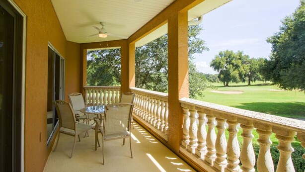 A covered balcony with a table and chairs, overlooking a golf course. - Apartment Live Oak Landing (Inverness)