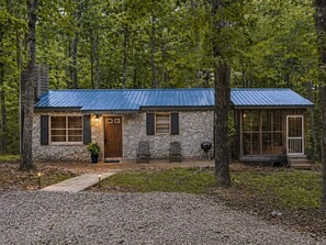 A rustic stone house with a blue metal roof, a front door, and a small porch area.