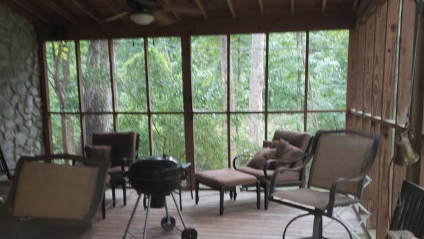 Un espace extérieur abrité, aménagé avec un barbecue, des chaises et un mur en pierre.