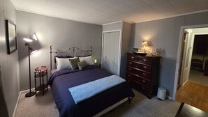 Une chambre à coucher comprenant un lit, une lampe de chevet, une commode et une porte donnant sur une autre pièce.