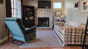 Un salon avec une cheminée, un canapé, un fauteuil et une bibliothèque.