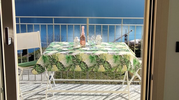 Un balcón con una mesa para dos, con vistas a un lago y montañas.