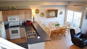 Una cocina con armarios de madera, microondas, horno y comedor con mesa y sillas.