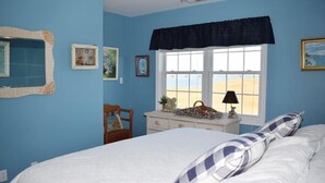 Un dormitorio con cama, cómoda, silla y ventana con vista a la playa.