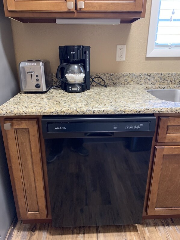 Una cocina con encimera de granito, un tostador, una cafetera y un lavavajillas.