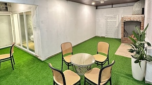 A room with a round table and four chairs, a ceiling fan, and a brick fireplace. - Emerald Dove (Tirupattur)