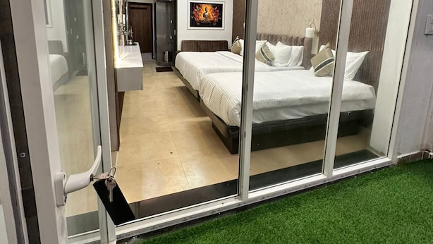 A modern bedroom with a glass door, a bed, a nightstand, a wall-mounted TV, and a ceiling fan. - Emerald Dove (Tirupattur)