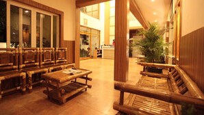 A lobby with wooden furniture, a large plant, and a view of the interior space. - Emerald Dove (Tirupattur)