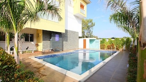 A swimming pool surrounded by a patio area with a modern building in the background. - Emerald Dove (Tirupattur)