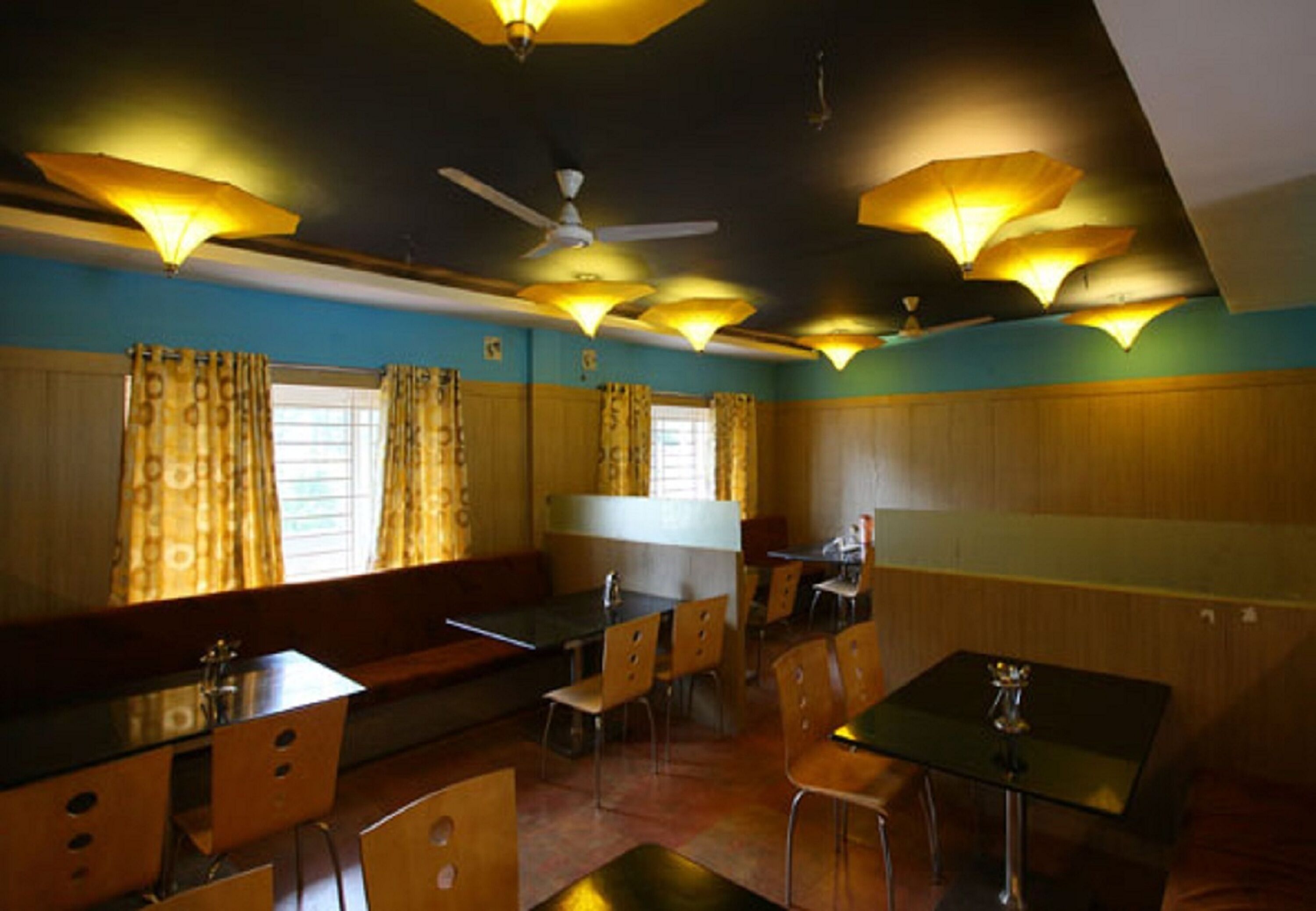Un restaurante con cabinas, mesas y una barra. Hay ventiladores de techo y lámparas colgantes.