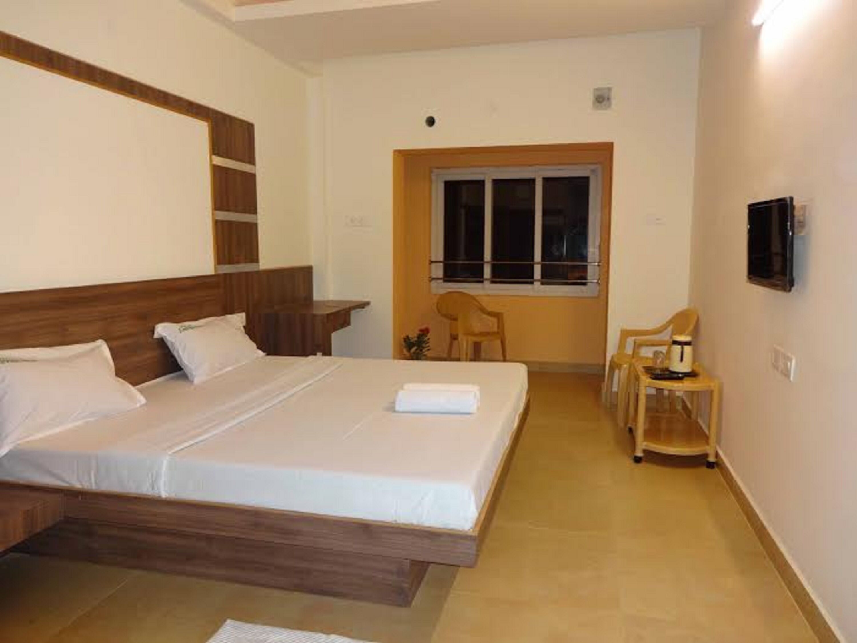 A bedroom with a wooden bed frame, a bedside table, a chair, and a TV mounted on the wall.
