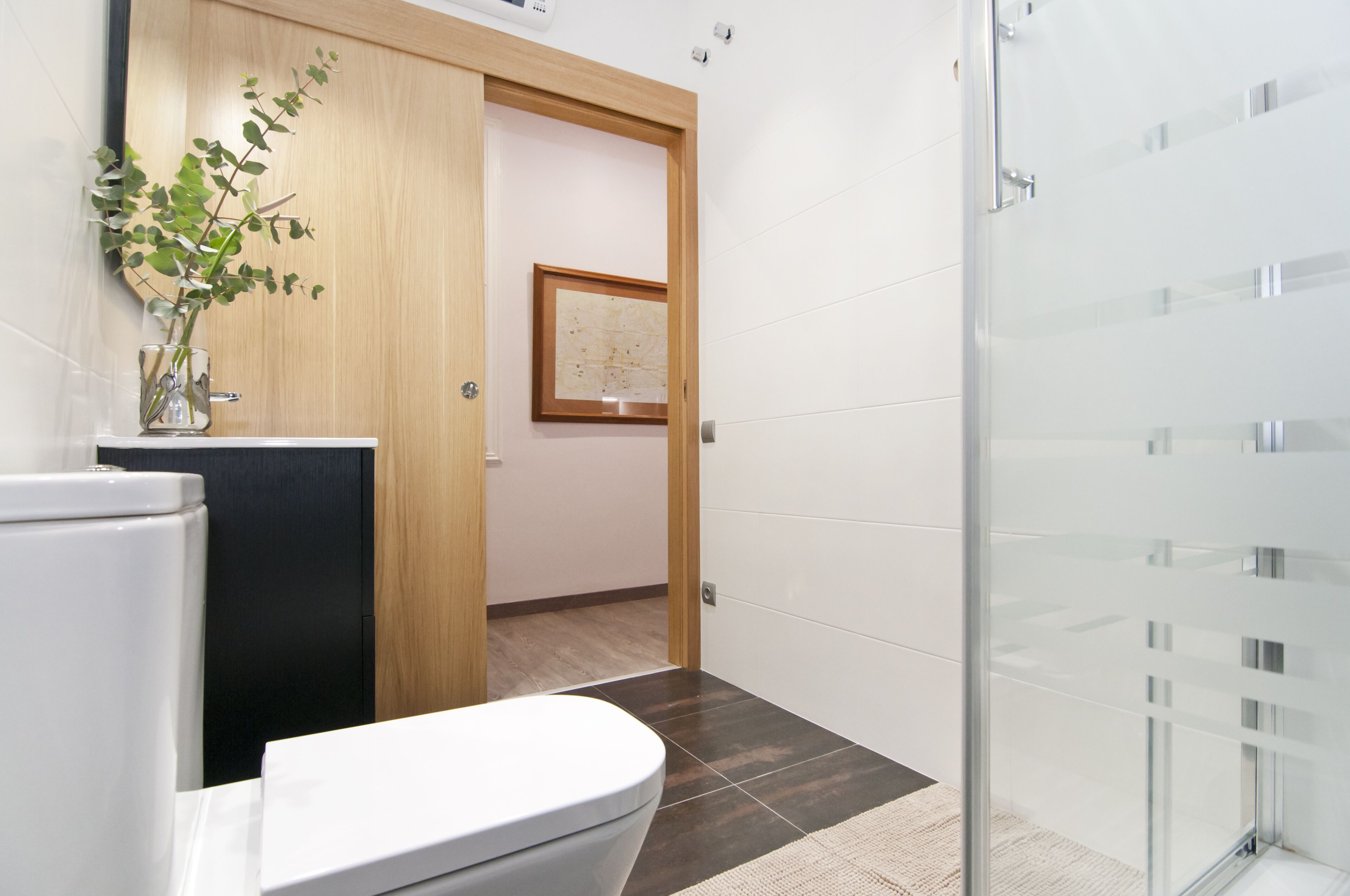 A modern bathroom with a toilet, a glass shower enclosure, and a wooden door leading to a hallway.