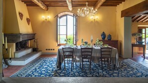 Ein Esszimmer mit großem Tisch für sechs Personen, Holzbalken an der Decke, einer Kronleuchter und einem Kamin mit Sims.
