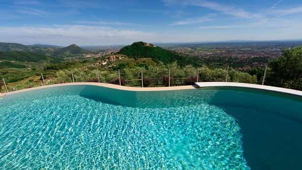 Ein klarer, blauer Infinity-Pool mit Blick auf einen grünen Hügel und eine entfernte Stadt.