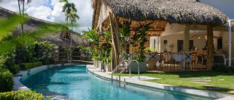A swimming pool with a thatched-roof structure and outdoor seating area.
