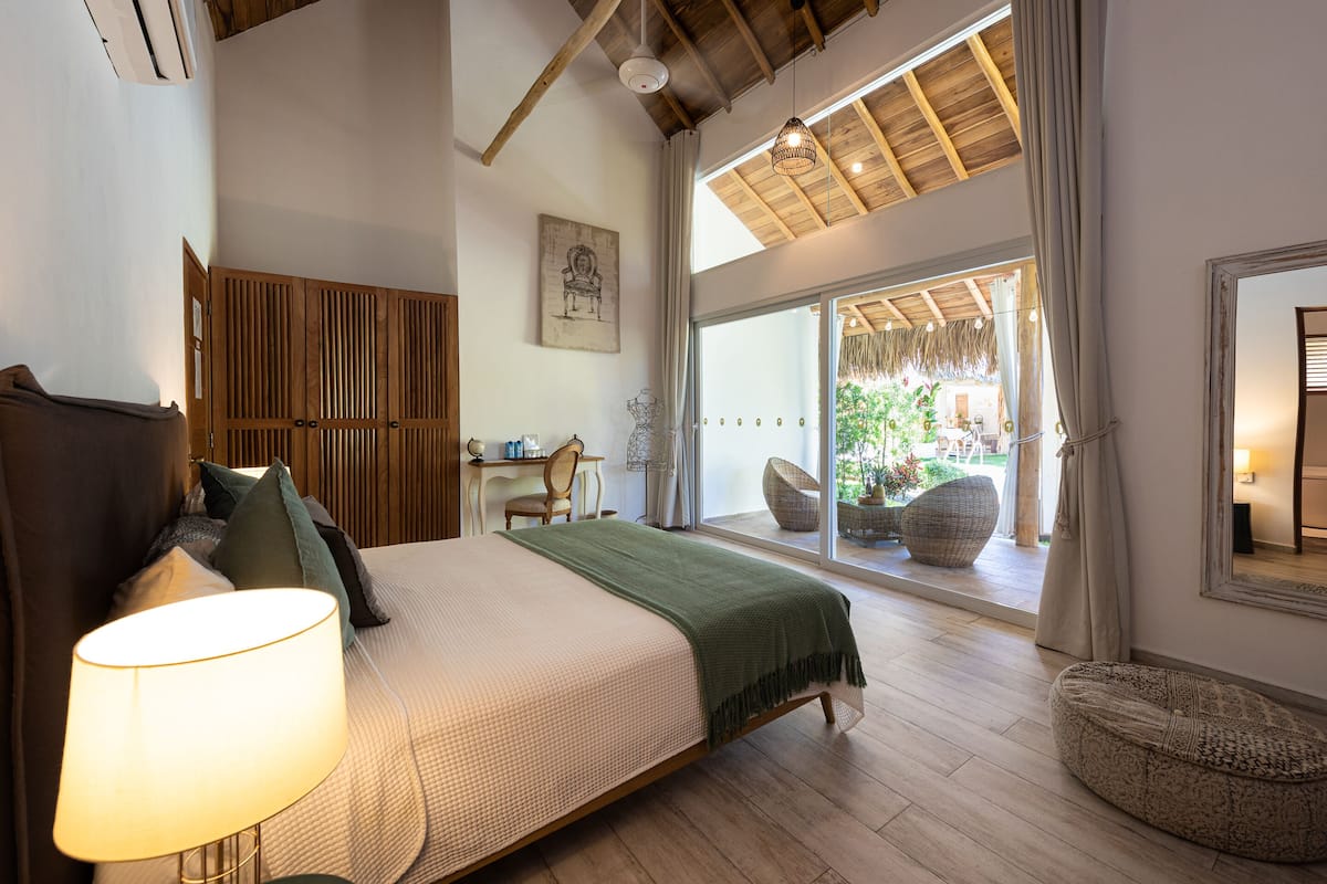 A bedroom with a bed, a desk, and a view of the outdoors.