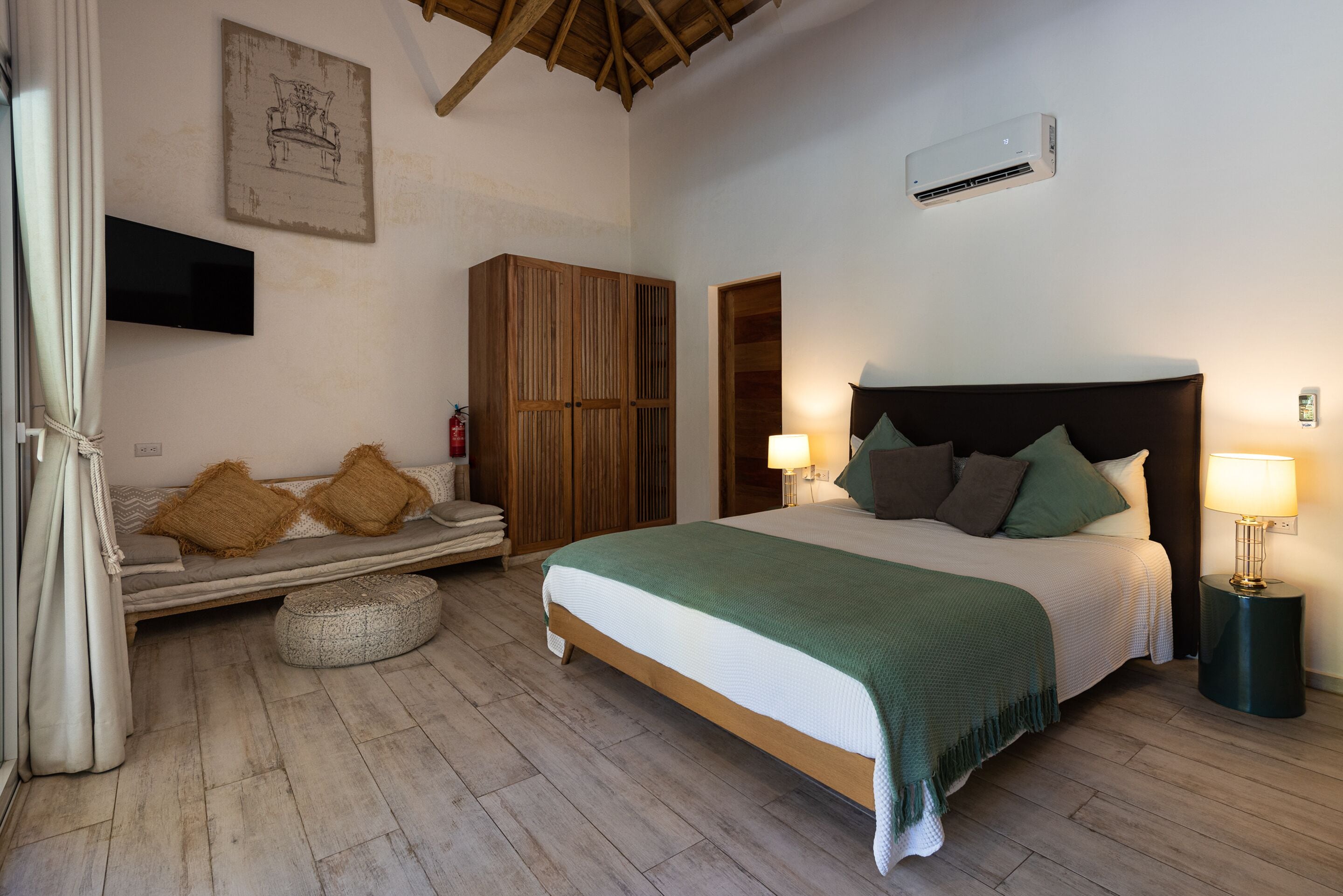 Un dormitorio con cama, lámparas de noche, un armario de madera, televisor y aire acondicionado instalado en la pared.