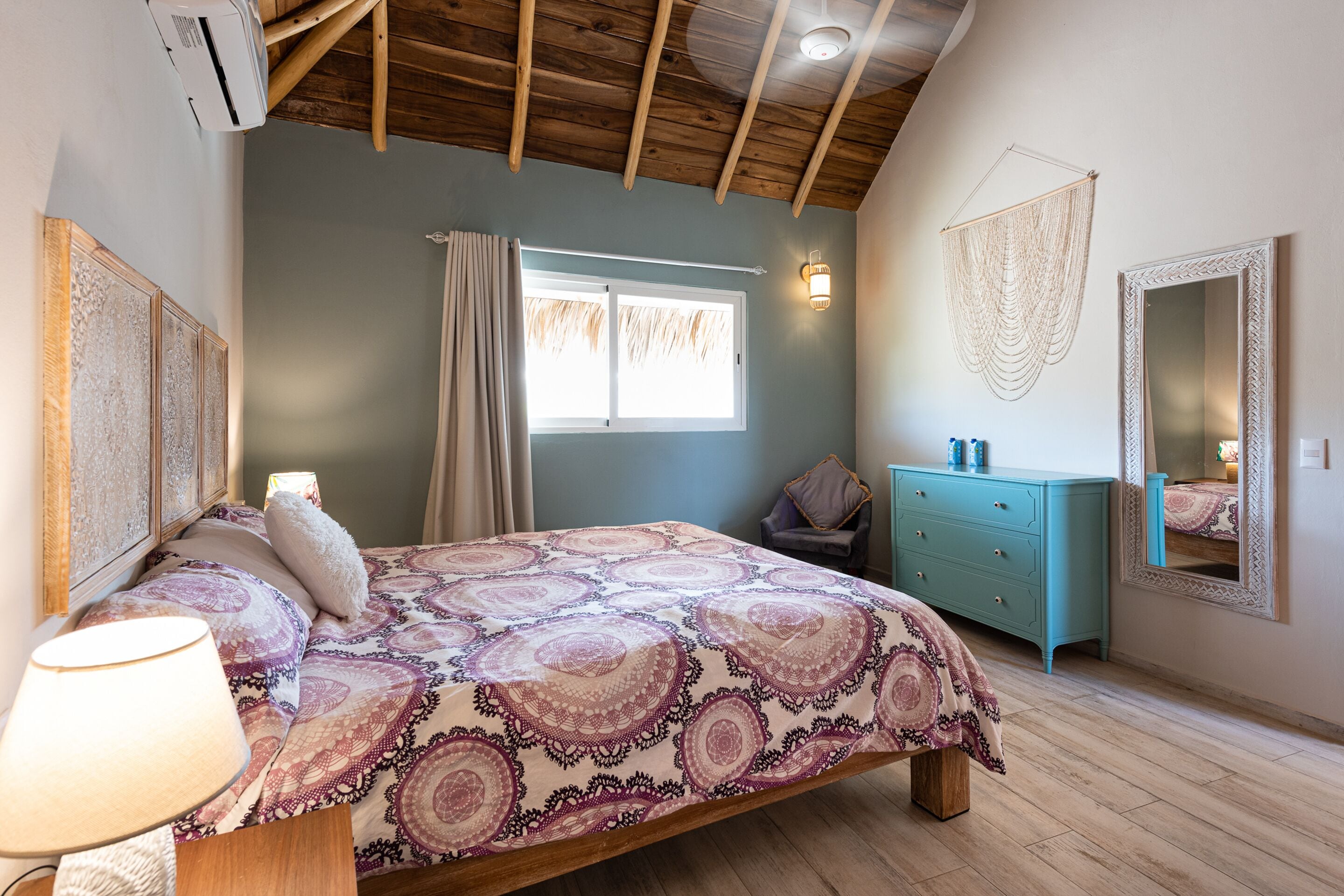 A bedroom with a bed, a dresser, a mirror, and a window with curtains.