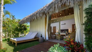 A thatched-roof bungalow with a wooden deck, a lounge area with a single bed, and a bathroom with a large mirror and wicker furniture. - Takuma Boutik Hotel (Las Terrenas)