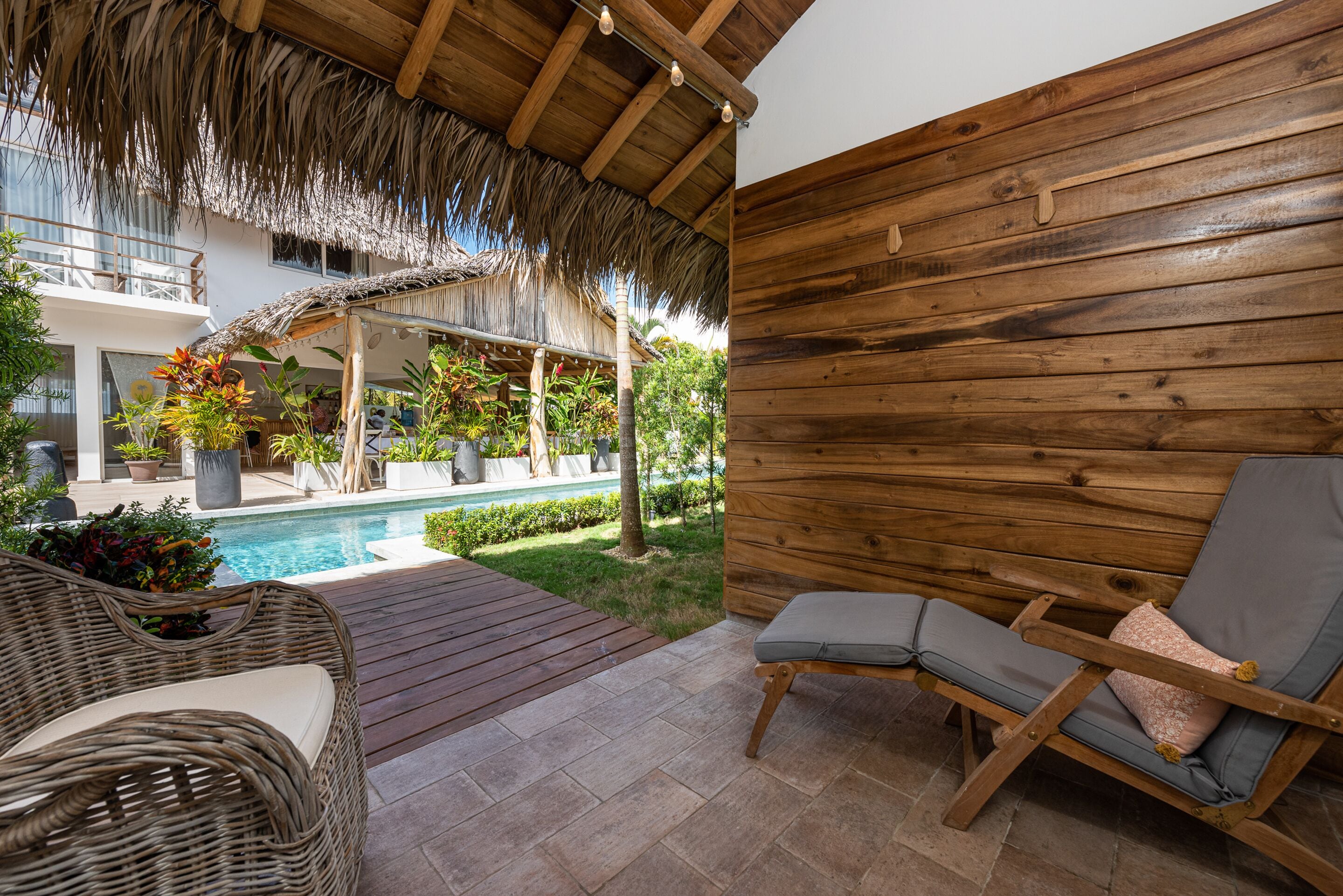 Um deck de madeira com piscina, móveis de vime e uma cobertura de palha.
