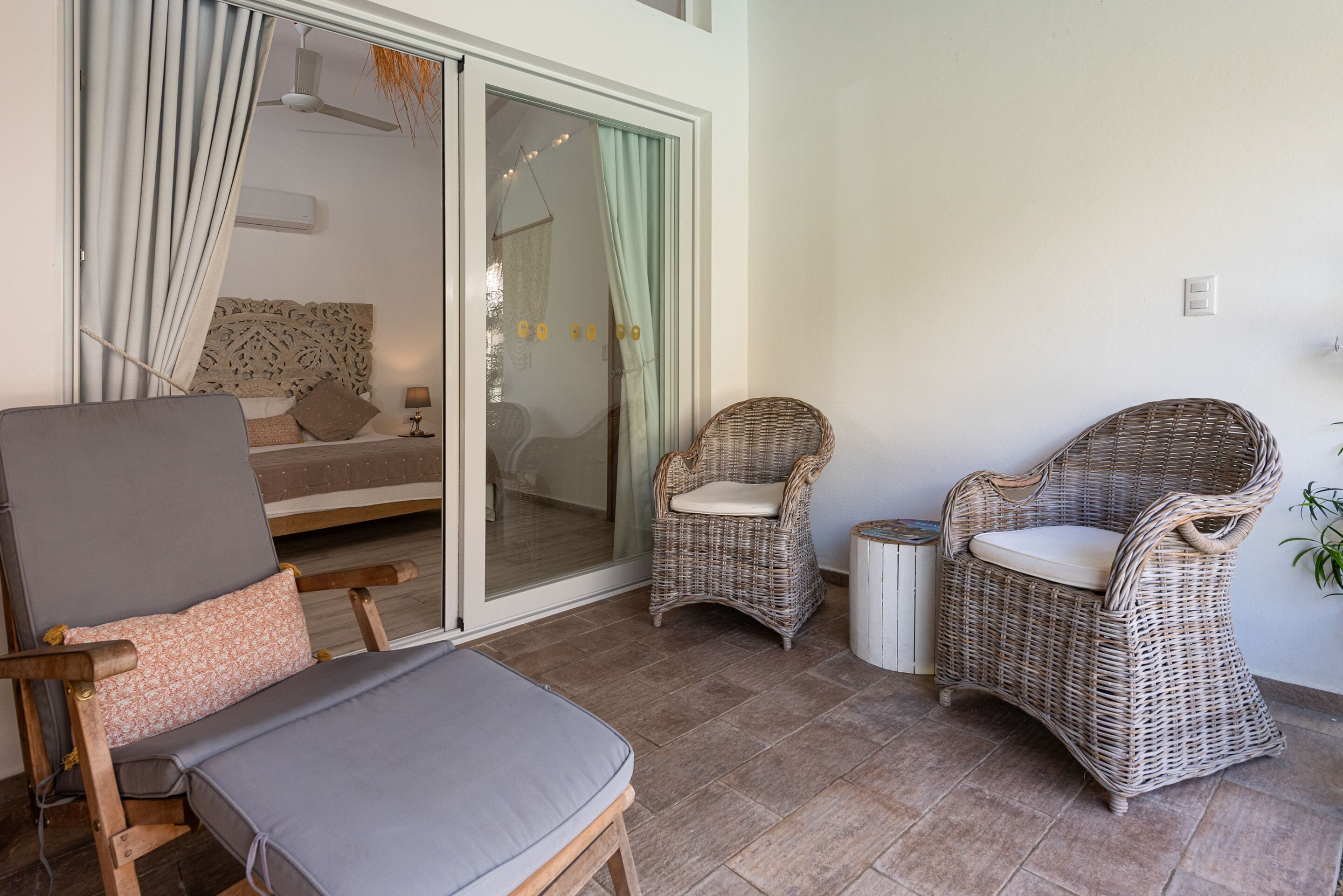 A room with a bed, a grey sofa, wicker chairs, and a small table.