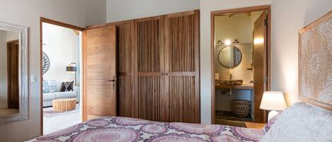 A bedroom with a bed, wooden wardrobe, and a bathroom visible through an open door.