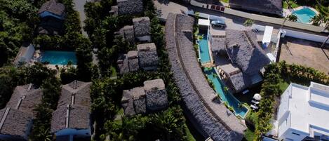 An aerial view of a resort with thatched-roof buildings, a central swimming pool, and lush greenery.