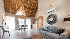 A spacious living area with a wooden ceiling, a grey sofa, a round wooden coffee table, and a dining area with a table and chairs. - Takuma Boutik Hotel (Las Terrenas)