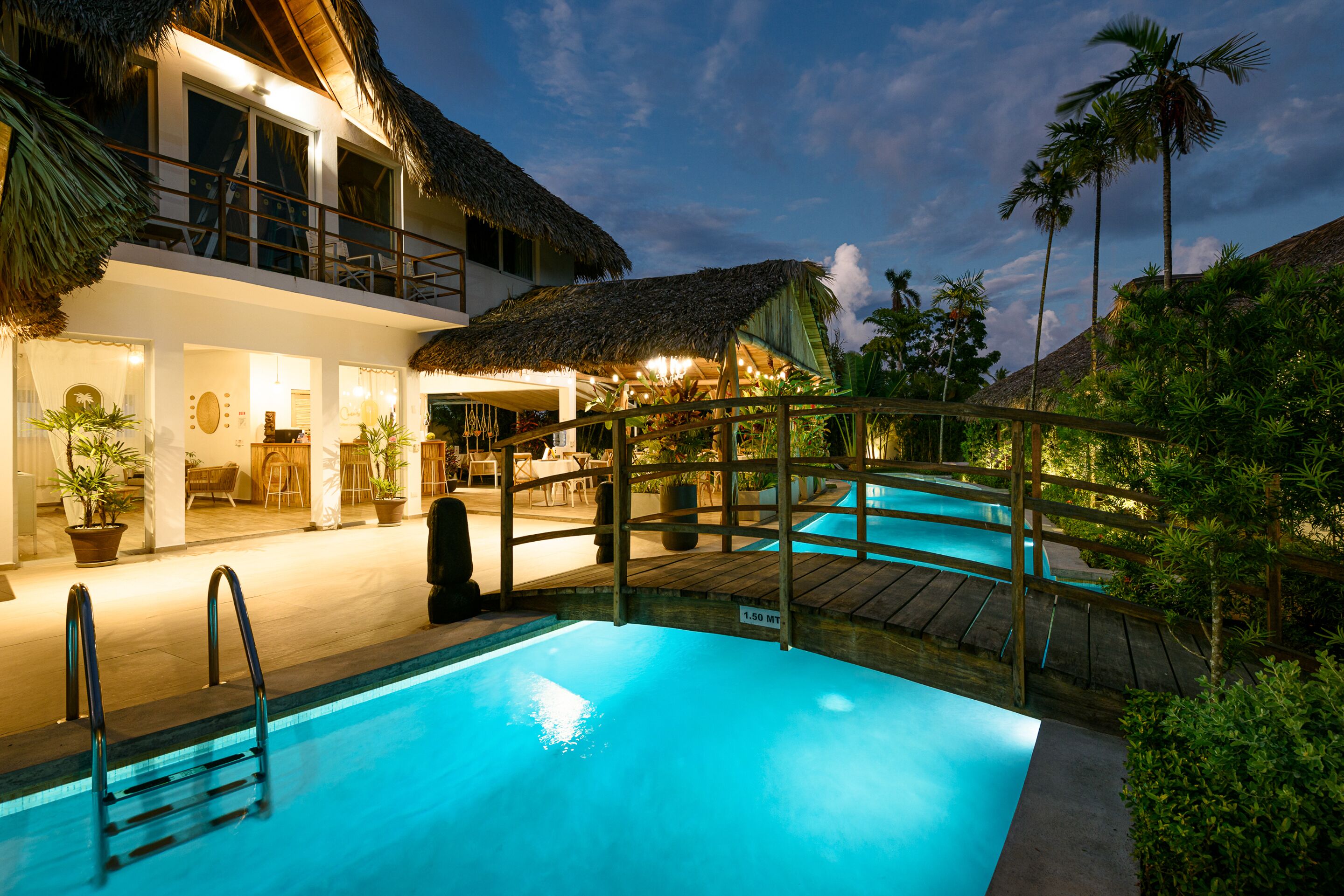 Zona de piscina con terraza de madera y estructura cubierta de paja.