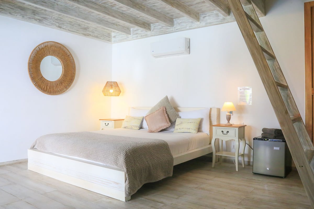 A bedroom with a bed, bedside tables, a lamp, a mirror, a radiator, and a wooden ladder.
