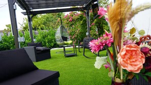 Una terrazza esterna con una poltrona amaca, un divano nero e un tavolo da pranzo.
