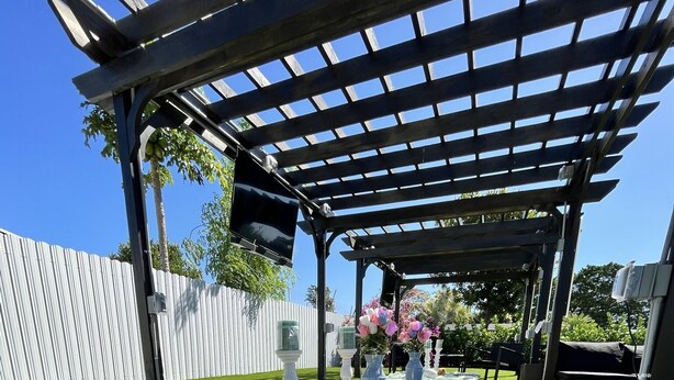 Un'area relax esterna coperta, con pergola, prato sintetico e arredi da giardino.