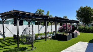Un'area patio con un pergolato, posti a sedere all'aperto e prato artificiale.