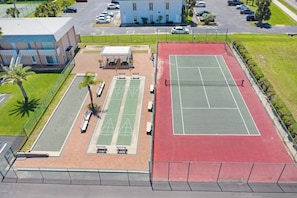An aerial view of a sports facility with a tennis court, a covered seating area, and a building in the background.