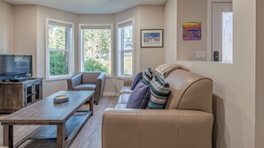 A living room with a sofa, a coffee table, a TV, and large windows. - Family Orientated Lower Knoll Chalet All to Yourself w/Hot Tub, Laundry, BBQ (Silver Star Mountain)