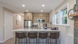 A modern kitchen with a central island, bar stools, stainless steel appliances, and a clock on the wall. - Family Orientated Lower Knoll Chalet All to Yourself w/Hot Tub, Laundry, BBQ (Silver Star Mountain)