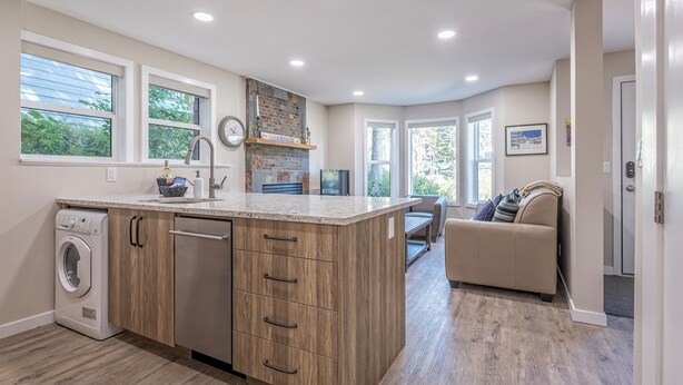 A modern kitchen with a built-in washer and dryer, wooden cabinetry, and a large island with a sink. - Family Orientated Lower Knoll Chalet All to Yourself w/Hot Tub, Laundry, BBQ (Silver Star Mountain)