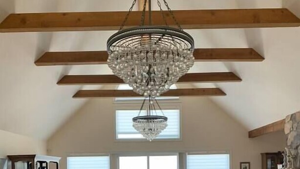 A spacious living room with a high ceiling, wooden beams, a large chandelier, a sofa set, and a stone fireplace. - Villa Alta Vista at Yosemite- Mtn Views, Game Room, Pool Table, Deck, Sleeps 10+ (Mariposa County)