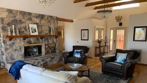 A spacious living room with a stone fireplace, leather sofas, and a chandelier. - Villa Alta Vista at Yosemite- Mtn Views, Game Room, Pool Table, Deck, Sleeps 10+ (Mariposa County)