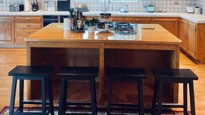 A kitchen with wooden cabinets, a central island with stools, pendant lighting, and a tiled backsplash. - Villa Alta Vista at Yosemite- Mtn Views, Game Room, Pool Table, Deck, Sleeps 10+ (Mariposa County)