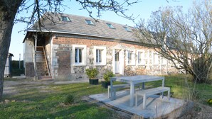 Ein Gebäude aus Stein mit einem geneigten Dach, einer Holztreppe und einem kleinen Garten mit einer Bank.