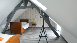 Ein kleines Schlafzimmer im Mansardenstil mit schrägen Wänden, einem hölzernen Bett, einem kleinen Tisch und einer Stehlampe.